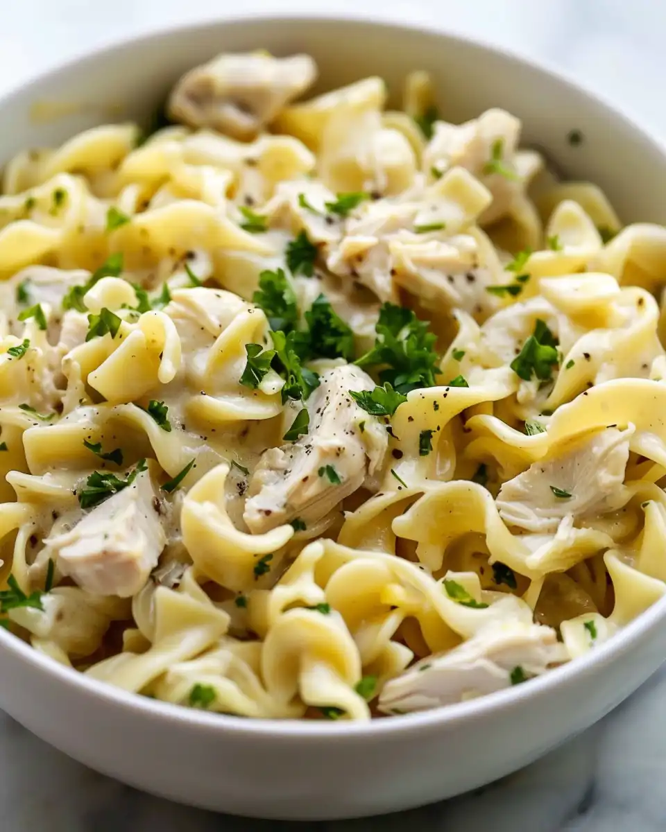 Plated parmesan chicken resting on buttered egg noodles with seasoning herbs